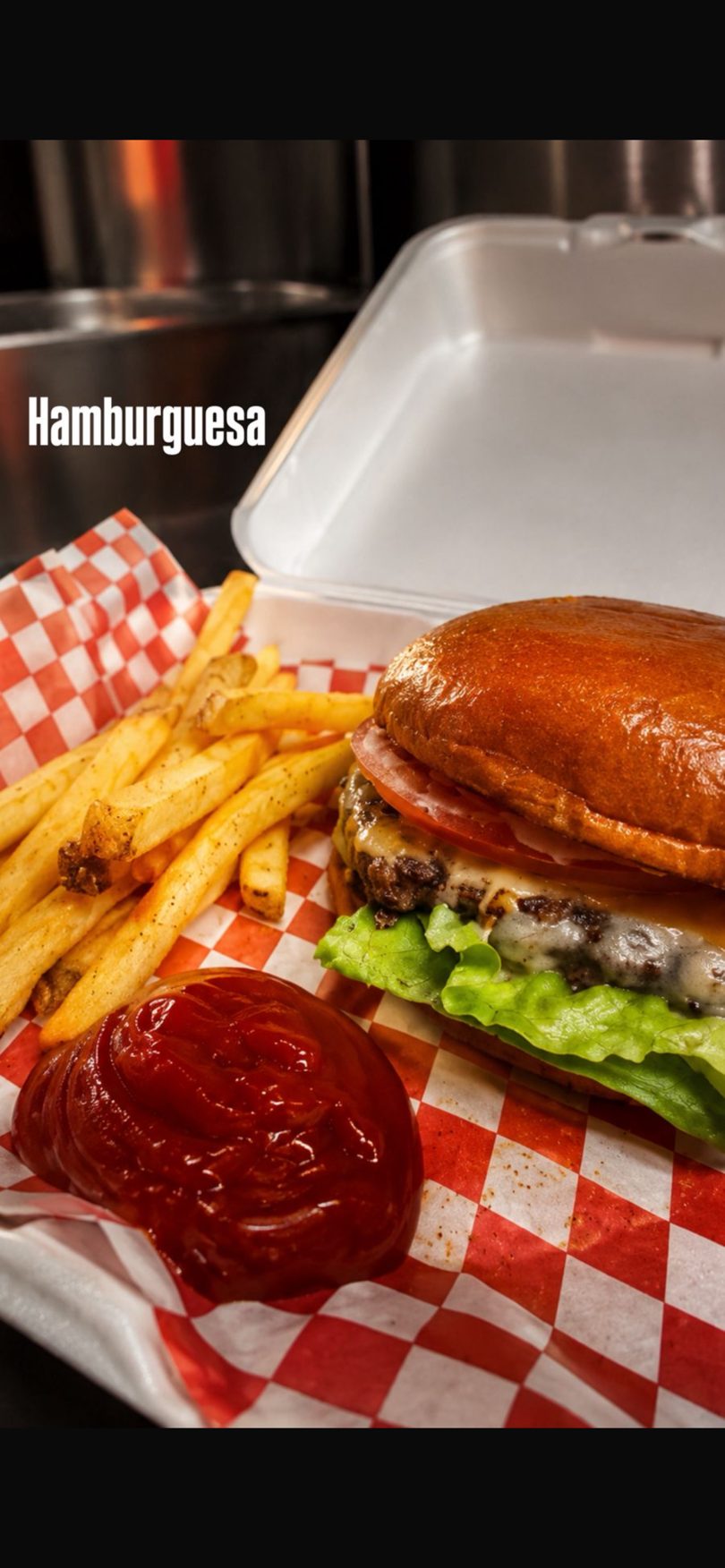 Cheeseburger with lettuce, tomato, and fries with ketchup, served in a red and white checkered basket.